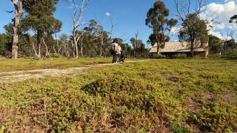 Two-women-are-walking-along-a-dirt-path-towards-an-old-house-in-the-bush