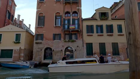 Boat-transporting-tourists-passing-on-the-canal-while-the-rainbow-flag-is-displayed-on-a-balcony-in-the-background