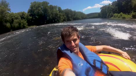 A-static-shot-of-a-man-recording-himself-by-his-mobile-phone-while-floating-down-a-river-in-a-blow-up-tube-with-a-in-summer-day