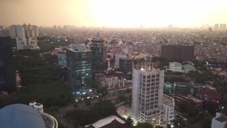 Schwenken-Der-Skyline-Der-Stadt-Jakarta,-Während-Die-Sonne-Untergeht-Und-In-Die-Kamera-Strahlt,-Wobei-Das-Am-Weitesten-Entfernte-Gebäude-Im-Licht-Verborgen-Ist