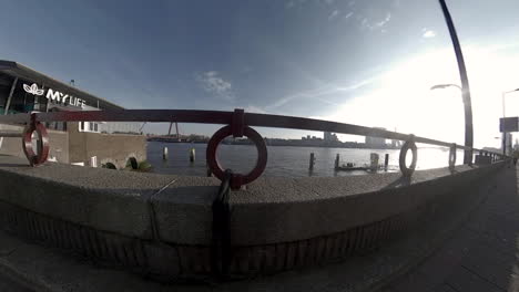 Chica-Corriendo-En-El-Paseo-Marítimo-Del-Nuevo-Río-Mosa-En-Rotterdam,-Países-Bajos---Vista-De-Ojo-De-Pez-Desde-El-Anillo-De-Barandilla---Retroceso