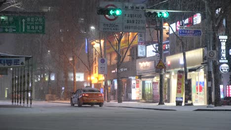 Heavy-snow-falls-in-Seoul-as-a-taxi-drives-down-a-shopping-street,-South-Korea