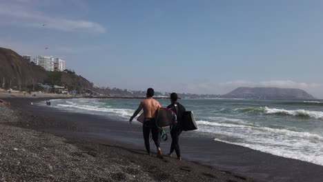 4k-daytime-video-with-2-surfers-walking-on-the-beach-shores-of-Miraflores,-Lima,-Peru