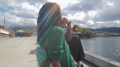 Mujer-Afro-Con-Pelos-Rizados-Sentada-Relajándose-Sola-En-Un-Banco-Al-Aire-Libre-Frente-Al-Mar-En-El-Muelle-Del-Puerto-Deportivo,-Port-Alberni,-Columbia-Británica,-Canadá