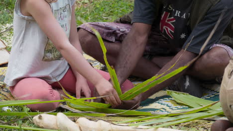 Kanak-man-shows-young-caucasian-girl-palm-fronds-weaving-on-Maré,-New-Caledonia