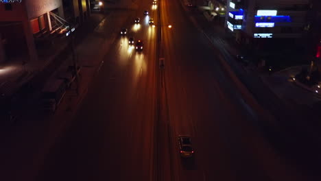 Seguimiento-De-Imágenes-Aéreas-Siguiendo-A-Un-Coche-Por-Una-Concurrida-Calle-Urbana-Por-La-Noche