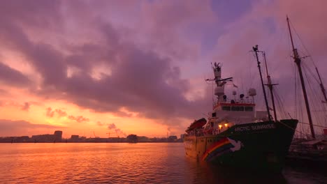 Tracking-shot-of-Greenpeace-ship-the-Arctic-Sunrise,-docked-on-the-IJ-river-in-Amsterdam,-against-a-beautiful-sunrset-background