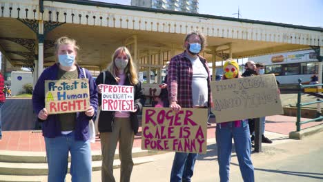 group-of-four-people-standing-together-with-cards-wearing-masks-attending-for-a-peaceful-protest-by-the-seaside