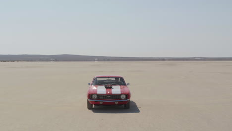 Toma-Aérea-De-Un-Auto-Mustang-De-Color-Rojo-Y-Blanco-En-El-Desierto