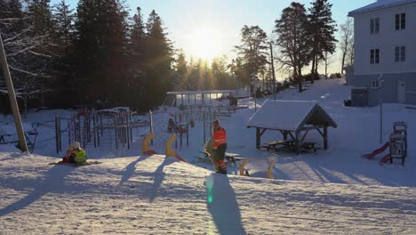 Hermosas-Luces-De-La-Mañana-Sobre-El-Patio-De-Juegos-De-Invierno-Con-Niños-Jugando-Y-Gente-Caminando