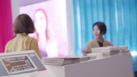 Women-working-kiosk,-in-uniform,-standing-behind-brochures,-half-body-shot