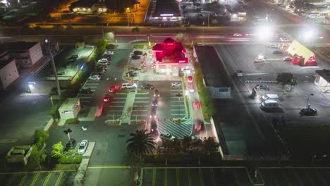 Zeitraffervideo-Einer-Drohne-Von-Autos,-Die-Sich-Vor-Dem-In-and-Out-Restaurant-Zum-Abendessen-Anstellen.-Die-Hellen-Lichter-Streifen-Und-Erhellen-Die-Nacht,-Während-Die-Leute-Darauf-Warten,-An-Die-Reihe-Zu-Kommen,-Um-Eine-Köstliche-Mahlzeit-Zu-Genießen.