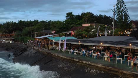 Menschen,-Die-Bei-Sonnenuntergang-In-Einem-Restaurant-Am-Meer-Am-Echo-Beach-In-Canggu-Bali-Speisen,-Aus-Der-Luft