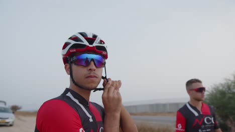 Un-Joven-Atleta-Profesional-Se-Pone-El-Casco-Mientras-Su-Amigo-Detrás-De-él-Mira-Hacia-Adelante.