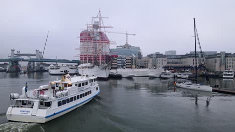 Ferry-Cruising-Towards-The-Port-Of-Lilla-Bommen-With-View-Of-The-Viking-And-The-Lipstick-Building-In-Gothenburg,-Sweden---low-aerial