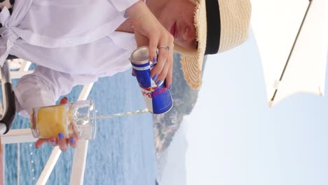 Young-blonde-girl-with-a-straw-hat-pours-Redbull-into-a-glass-with-ice-cubes-at-the-Old-Town-restaurant-in-Dubrovnik,-Croatia