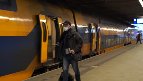 Handheld-shot-of-a-man-in-a-mask-running-to-catch-the-train,-pulling-a-suitcase