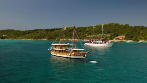 Young-adult-jumping-off-bow-of-sailboat-ship-into-tropical-sea,-aerial-pull-away