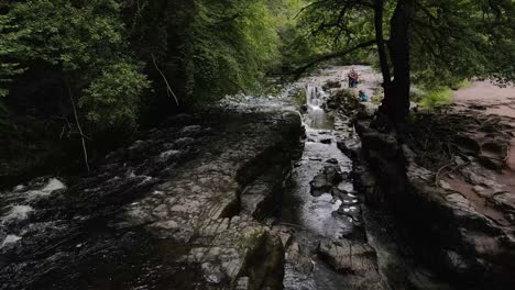 Brecon-Beacons-rocky-river-flowing-water-idyllic-uncultivated-low-aerial-flying-through-welsh-woodland-wilderness