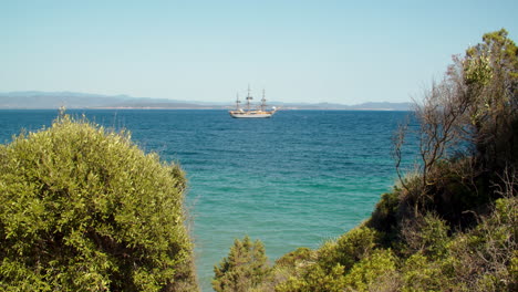 Paradisiac-view-of-Sardinian-turquoise-cristal-clear-sea-with-Italian-Amerigo-Vespucci-ship-in-background,-most-beautiful-ship-in-the-world,-static,-sunny-summer-day