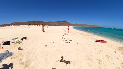 A-group-of-friends-throw-around-a-yellow-American-football-on-a-white-sand-beach-in-Mexico