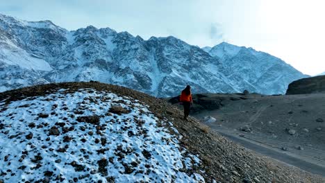 Vista-Aérea-De-Un-Niño-Bajando-Una-Colina-Con-Una-Variedad-De-Montañas-Cubiertas-De-Nieve-Al-Fondo-En-Skardu,-Pakistán