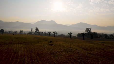 Aerial-flying-over-farm-fields-toward-mist-shrouded-mountains-in-Thailand