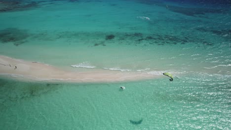 Kitesurfer-Reitet-über-Türkisfarbenes-Wasser-In-Der-Nähe-Einer-Sandigen-Landenge,-Luftaufnahme