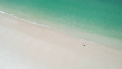 Aerial-View-of-Woman-Walking-on-White-Sand-Beach-by-Turquoise-Ocean-Water,-Tropical-Paradise-Destination