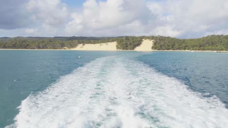 Wake-of-a-boat-on-turquoise-waters-heading-towards-sandy-shores-of-Moreton-Island,-Australia