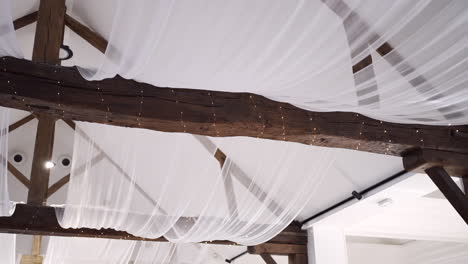 Exposed-wooden-beams-with-elegant-white-fabric-draping-in-an-airy-ceiling-decor