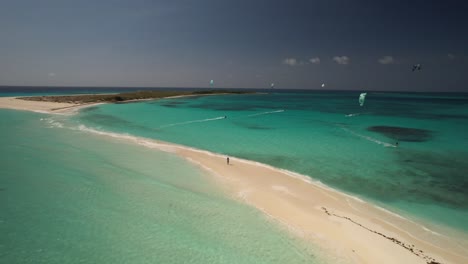 Kiteboarder-Reitet-Auf-Türkisfarbenen-Wellen-An-Einem-Unberührten-Sandstrand-Unter-Einem-Klaren-Blauen-Himmel