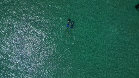 Top-down-drone-shot-above-two-scuba-divers-in-shallow-waters-of-Greece,-sunny-day