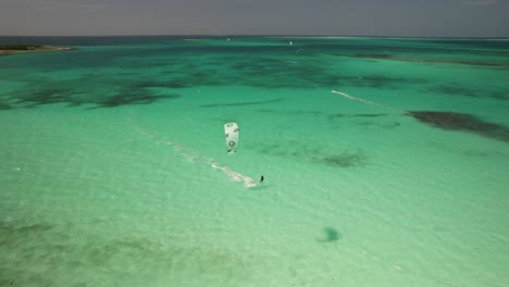 A-kite-surfer-glides-over-clear-turquoise-waters-near-an-island-under-a-sunny-sky