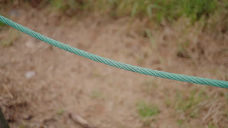 Close-up-of-a-turquoise-rope-stretched-across-a-sandy-and-grassy-background