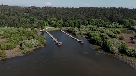 Aerial-of-wooden-decks-at-Pateira-de-Fermentelos-in-Aveiro,-Portugal,-surrounded-by-lush-greenery-and-calm-waters