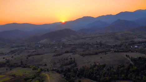 Scenic-aerial-view-of-the-sun-setting-behind-the-mountains-of-Pai,-Thailand