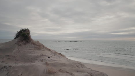 Wind-sculpted-sand-dune-by-a-calm-sea-under-a-cloudy-sky,-creating-a-serene-coastal-scene