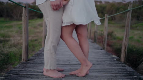 Close-up-of-barefoot-couple-standing-on-a-wooden-bridge,-holding-hands