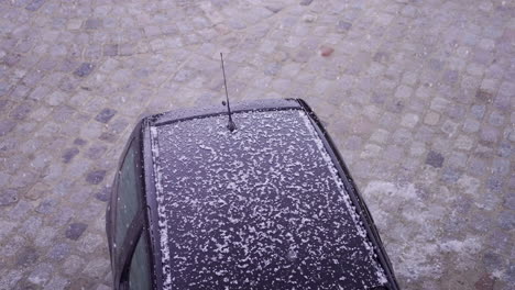 Intense-hail-falling-on-a-car-parked-on-a-cobblestone-street