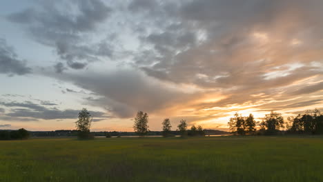 Sunset-light-recedes-across-grassy-field-as-clouds-race-across-soft-smooth-sky