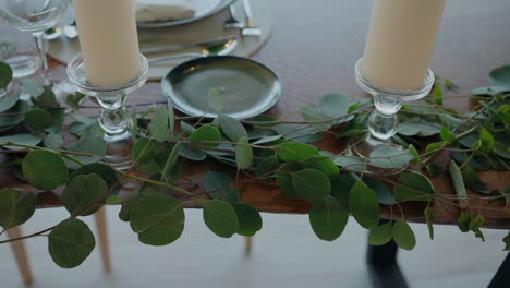 Mesa-Elegante-Con-Guirnaldas-De-Hojas-Verdes,-Velas-Y-Vajilla-Elegante