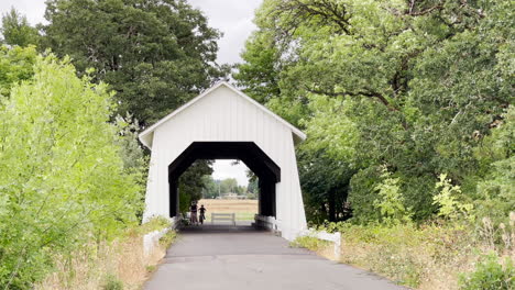 Two-people-on-bicycles-ride-through-a-covered-bridge-in-Corvallis,-Oregon