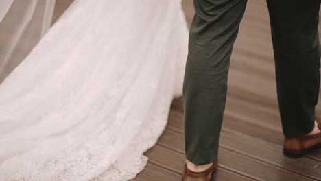 Close-up-of-a-bride-in-a-white-gown-and-a-groom-walking-together-on-a-wooden-deck