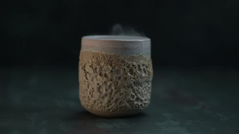 Rising-smoke-over-a-ceramic-glass-with-volcano-texture-on-the-dark-background