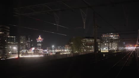 Exterior-train-view-of-Amsterdam's-railway,-Adam-toren,-A'DAM-tower-and-illuminated-city-in-the-background-during-night-time