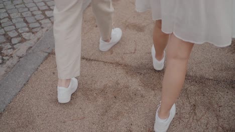 Close-up-of-a-couple-walking-on-a-sandy-path,-wearing-white-shoes-and-light-colored-clothing