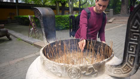 Caucasian-man-puts-incense-sticks-in-a-burner-at-North-Temple-in-Suzhou,-China