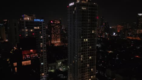 Illuminated-Buildings-And-Skyscrapers-In-Bangkok,-Thailand-At-Night---Aerial-Drone-Shot