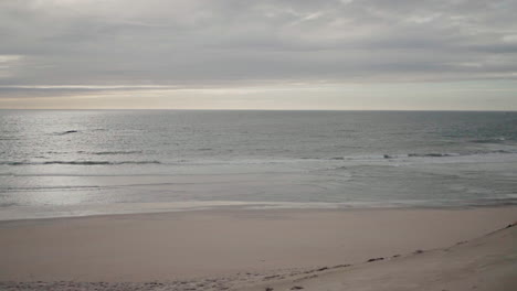 Calm-beach-with-gentle-waves-under-a-cloudy-sky,-creating-a-serene-coastal-atmosphere